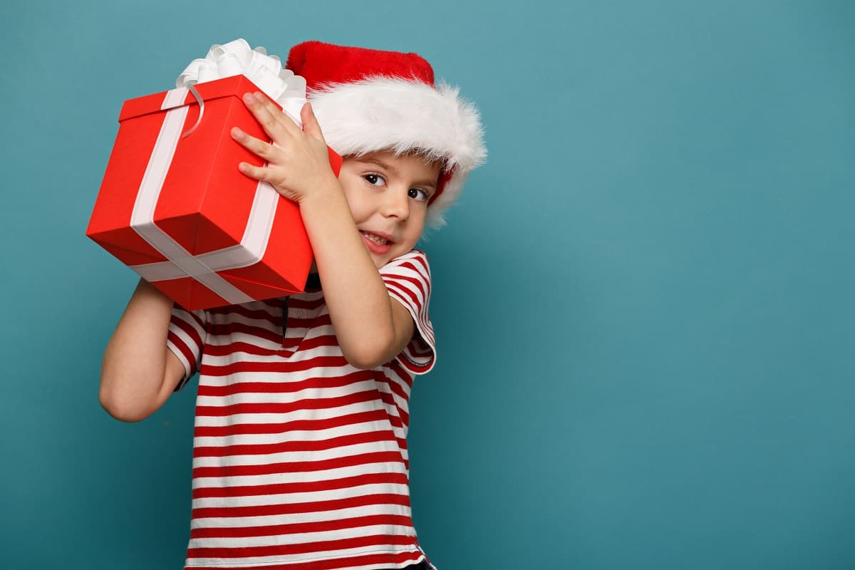 Funny child in Santa red hat holding Christmas gift in hand.