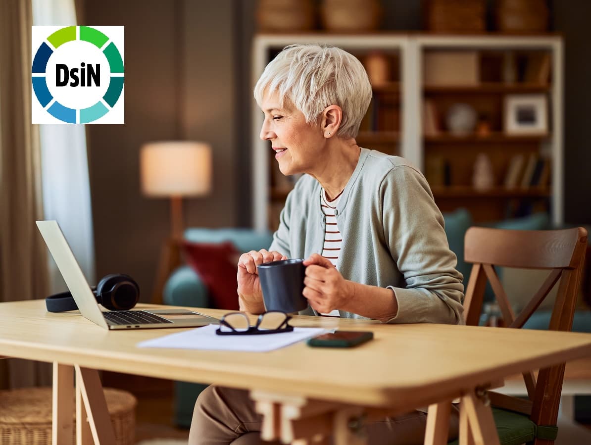 A focused senior adult woman working from home on a laptop and having a cup of coffee